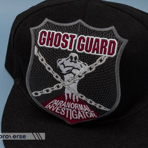 May include: Black baseball cap with a gray and red embroidered patch that says "Ghost Guard Paranormal Investigator" with a ghost figure in chains.