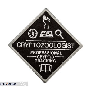 May include: Black and white embroidered patch in a diamond shape. The patch reads "Cryptozoologist" and "Professional Cryptid Tracking". It features a compass, footprint, and magnifying glass graphic.