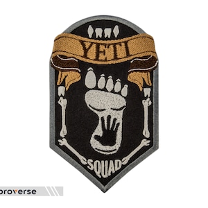 May include: A gray and black embroidered patch with a white footprint, a black handprint, and the text "YETI SQUAD" in a brown banner.