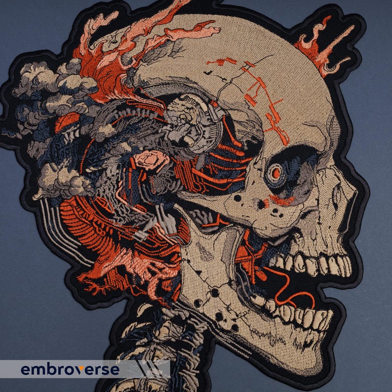 May include: Embroidered patch featuring a detailed, stylized skull with exposed internal components. The design incorporates shades of beige, black, orange, and gray, with a dark border. The text "embroverse" is visible at the bottom.