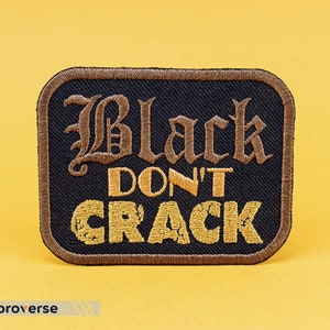 May include: Black embroidered patch with the text "Black Don't Crack" in gold thread on a black background.