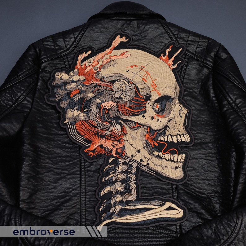 May include: Black leather jacket with a large embroidered patch featuring a detailed skull design. The patch incorporates shades of beige, orange, and blue, with intricate anatomical details and a skeletal structure. The jacket has a classic biker style.