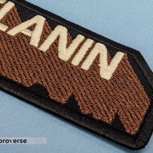 Peut inclure: Un patch brod&eacute; marron et blanc avec le mot "LANIN" en lettres blanches. Le patch a une bordure noire et un bord irr&eacute;gulier.