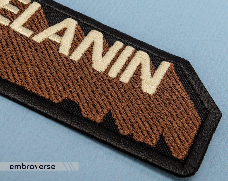 Peut inclure: Un patch brod&eacute; marron et blanc avec le mot "LANIN" en lettres blanches. Le patch a une bordure noire et un bord irr&eacute;gulier.