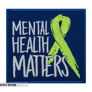 Pode incluir: Um remendo bordado azul com uma fita verde e o texto "Mental Health Matters" em branco.