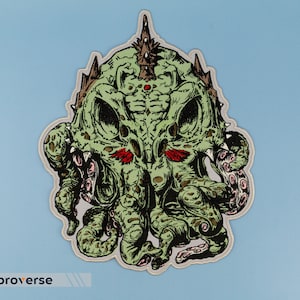 Op de afbeelding: Groen en rood geborduurd patch van een monsterlijk wezen met tentakels en een kroon. Het wezen heeft een dreigende uitdrukking en rode ogen.