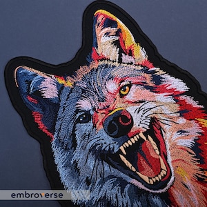 May include: A colorful embroidered patch of a wolf's head with its mouth open, showing sharp teeth. The wolf's fur is a mix of blue, red, yellow, and white.