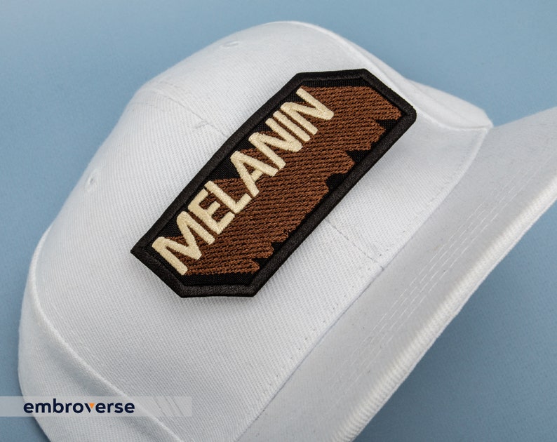 Peut inclure: Casquette de baseball blanche avec un patch brod&eacute; marron et noir qui dit "MELANIN" en lettres blanches.
