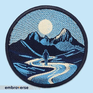 Peut inclure: Patch brodé avec une scène de montagne bleue et blanche. Une seule silhouette se promène sur un chemin sinueux au premier plan. La lune est visible dans le ciel.