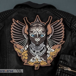 May include: A black leather jacket with a large embroidered patch on the back. The patch features a winged, stylised human figure with intricate details and blue eyes.