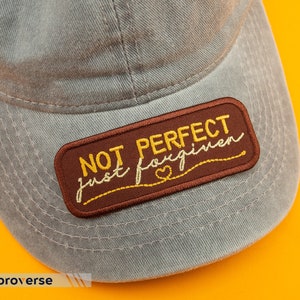May include: A grey baseball cap with a brown patch that says "NOT PERFECT just forgiven" in yellow embroidery.