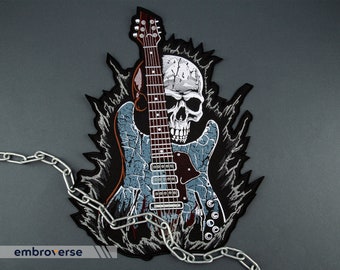 Puede incluir: Cráneo blanco y negro con una guitarra eléctrica azul y roja detrás. La guitarra y el cráneo están rodeados de llamas negras. Una cadena plateada está en primer plano.