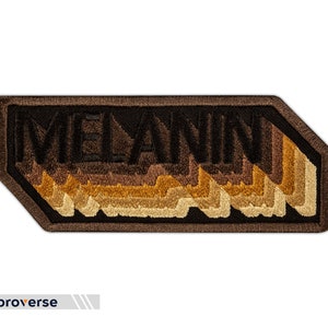 Peut inclure: Un patch brod&eacute; marron et noir avec le mot "MELANIN" dans un style 3D en couches. Les lettres sont soulign&eacute;es de noir et remplies de nuances de marron, beige et or.