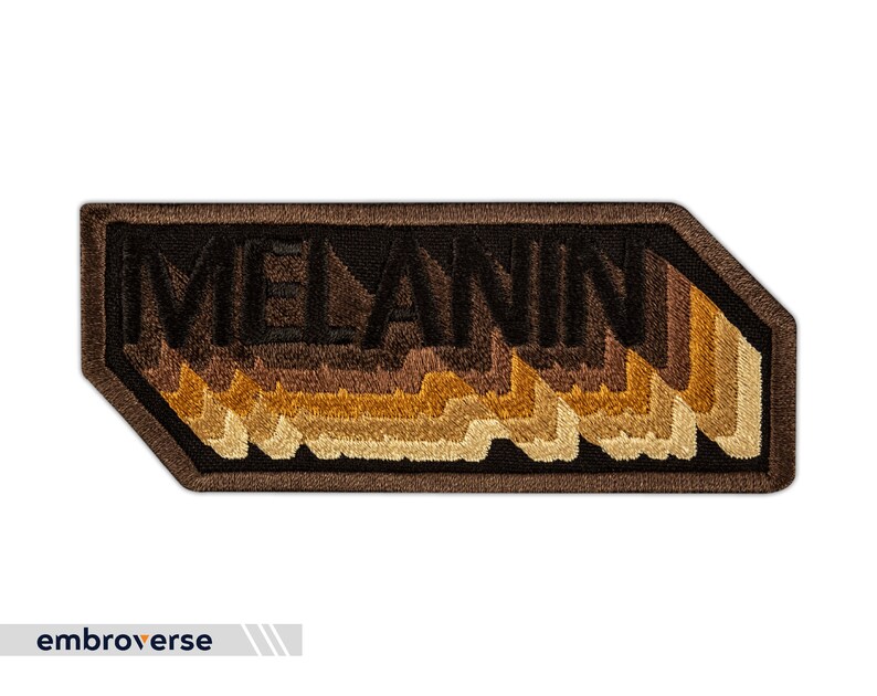 Peut inclure: Un patch brod&eacute; marron et noir avec le mot "MELANIN" dans un style 3D en couches. Les lettres sont soulign&eacute;es de noir et remplies de nuances de marron, beige et or.