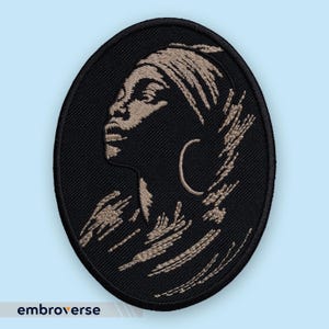 Peut inclure: Écusson brodé de forme ovale représentant le profil d'une personne portant un foulard et une boucle d'oreille. Le motif est en tons de beige et de noir, avec le texte "embroverse" en bas.
