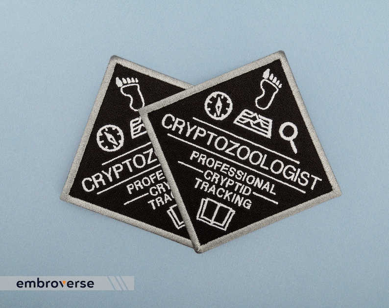 May include: Two black and silver embroidered patches with the text "Cryptozoologist - Professional Cryptid Tracking" and a compass, magnifying glass, footprint, and book graphic.