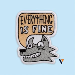 May include: An embroidered patch featuring a gray wolf head with a wide, toothy grin and wide eyes. Above the wolf is a tan speech bubble containing the black embroidered text "EVERYTHING IS FINE" in a hand-drawn style font with a white border.
