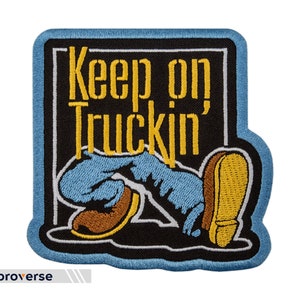 May include: A blue and black embroidered patch with the text "Keep on Truckin'" in yellow lettering. A cartoon illustration of a person's legs and feet are shown in the patch.
