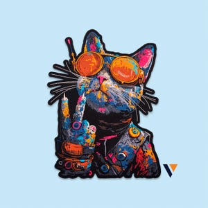 May include: A colorful embroidered patch featuring a cat wearing orange-tinted goggles and a vest. The cat is making a peace sign with one paw, which is adorned with a ring. The design uses vibrant splashes of blue, orange, pink, and yellow.