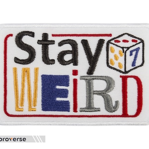 May include: White embroidered patch with red border. The patch says "Stay Weird" with a red, yellow, blue, and gray color scheme. A white dice with red dots and a blue "7" is in the upper right corner.