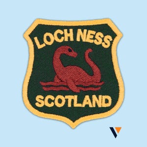 Op de afbeelding: Geborduurde patch in schildvorm met een gouden rand, met het Loch Ness Monster in roodbruin op een donkergroene achtergrond. De woorden "LOCH NESS SCOTLAND" staan in een boog boven en onder het monster.