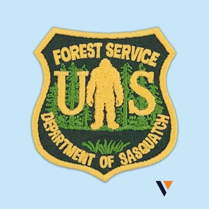 Peut inclure: Écusson brodé en forme de bouclier avec le texte "FOREST SERVICE" et "DEPARTMENT OF SASQUATCH". Bordure jaune et figure de Sasquatch jaune. Fond vert foncé.