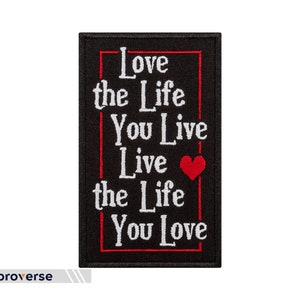 以下が含まれることがあります： 赤い縁取りと白い文字で「Love the Life You Live Live the Life You Love」と書かれた黒い刺繍パッチ。小さな赤いハートが描かれている。