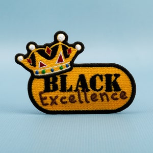 Peut inclure: Un écusson brodé jaune avec une couronne et le texte "BLACK Excellence".