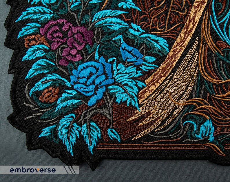 Puede incluir: Parche bordado con un dise&ntilde;o floral con flores azules, moradas y marrones sobre un fondo negro.
