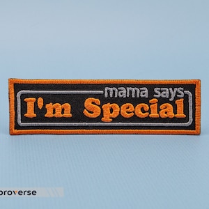 May include: Orange and grey embroidered patch with the text "mama says I'm Special" on a black background.
