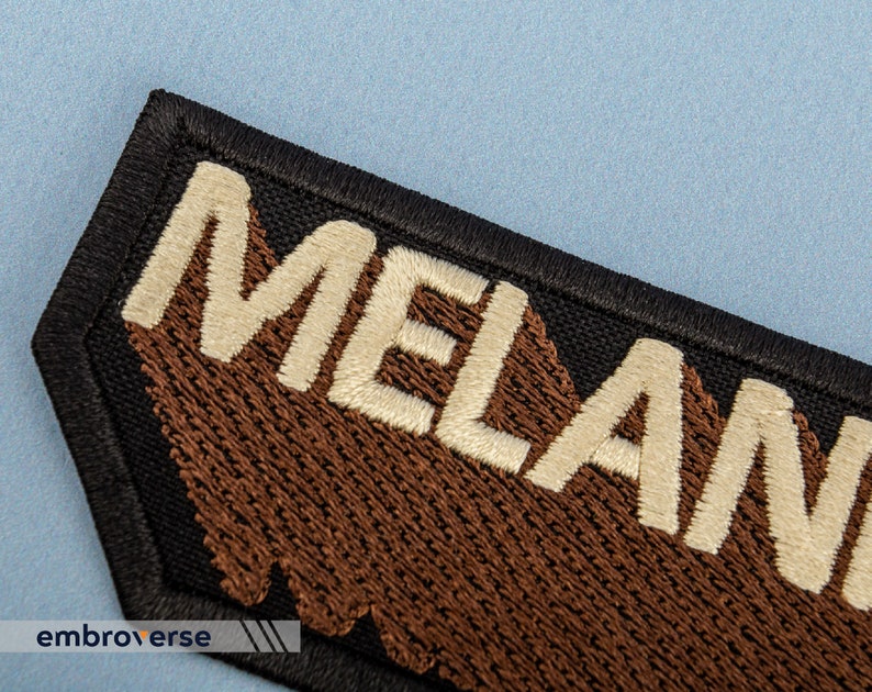 Peut inclure: Un patch noir avec des coutures brunes et le mot "MELANIN" brod&eacute; en blanc.