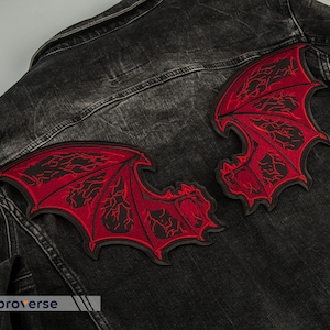 Könnte beinhalten: Eine schwarze Jeansjacke mit zwei roten gestickten Flecken von Dämonenflügeln auf dem Rücken.