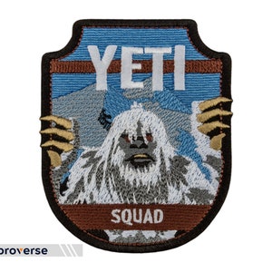 May include: Embroidered patch featuring a white Yeti with the text "YETI SQUAD" in white letters on a blue and brown background. The patch has a shield shape with a black border and gold accents.