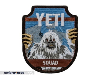 May include: Embroidered patch featuring a white Yeti with the text "YETI SQUAD" in white letters on a blue and brown background. The patch has a shield shape with a black border and gold accents.