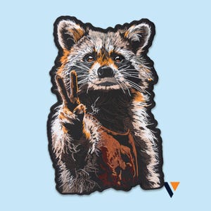 May include: Embroidered patch featuring a raccoon giving the peace sign. The raccoon has brown, black, and white fur, with a brown apron. The patch has a black border and is set against a light blue background.