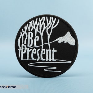 May include: Black embroidered patch with white text that reads "Be Present" and a stylized tree design.