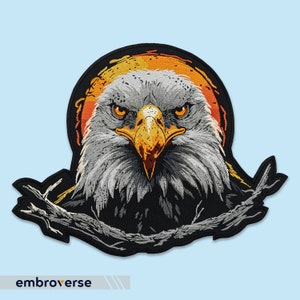 Puede incluir: Parche bordado de la cabeza de un águila calva sobre un fondo amarillo y naranja. El águila mira directamente al espectador con una expresión seria. El parche está rodeado por una rama marrón oscura.