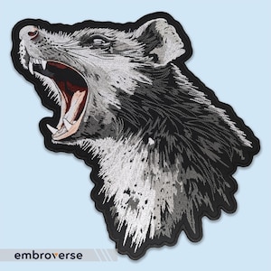 Peut inclure: Patch brodé noir et blanc d'une tête de loup grognant avec un fond blanc.