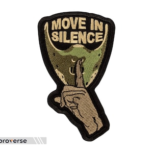 Pode incluir: Um remendo bordado preto e verde com uma mão segurando um dedo nos lábios. O remendo diz "Move in Silence".