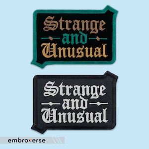 Peut inclure: Deux patchs brodés noirs avec des points blancs. Le patch du haut a le texte "Strange and Unusual" en fil doré et vert. Le patch du bas a le texte "Strange and Unusual" en fil blanc.