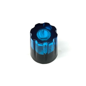 Puede incluir: Un pomo decorativo azul y negro con un diseño texturizado único. El pomo tiene una parte superior circular con una hendidura central y un borde acanalado. La parte inferior del pomo es negra, mientras que la sección superior es azul translúcido.