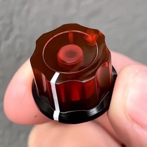 May include: A translucent amber-colored control knob with a fluted, gear-like edge and a flat top surface. The knob features a single vertical white indicator line running down the side and a circular indentation in the center of the top face.