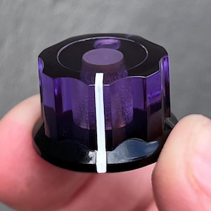 May include: A translucent purple plastic control knob with a fluted cylindrical shape and a solid black base. A single vertical white indicator line is printed on the side, extending from the top edge down to the bottom black rim of the knob.