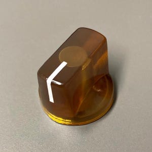 May include: A translucent amber-colored control knob with a cylindrical base and a rectangular top section. A single white indicator line is printed on the side and top surface of the knob to show the current position of the dial setting.