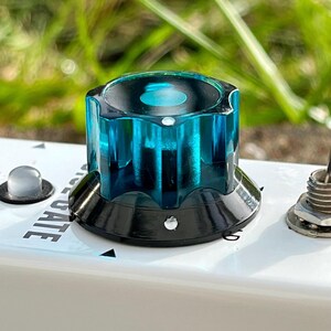 Puede incluir: Primer plano de un mando con una parte superior azul transparente y una base negra. El mando está sobre una superficie blanca con la palabra "GATE" visible. También se ven otros componentes.