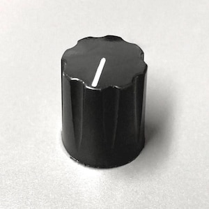 May include: A cylindrical black control knob featuring a scalloped edge and a single vertical white indicator line on the top surface. The knob has a series of vertical ridges along its side, providing a textured grip for manual adjustment.