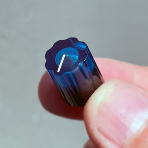 Op de afbeelding: Een blauwe plastic knop met een witte indicatorlijn. De knop heeft een geribbeld ontwerp.