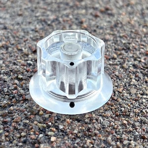 Könnte beinhalten: Ein klarer, facettierter Bedienknopf mit kreisförmiger Basis. Der Knopf hat eine zylindrische Mitte und eine Reihe vertikaler Rippen. Die Basis ist eine klare, flache Scheibe.