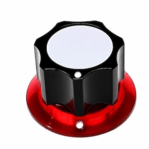 Pode incluir: Um botão de controlo preto com um topo circular branco e uma borda recortada, montado numa base circular vermelha translúcida. O botão preto apresenta um pequeno orifício na lateral e a base vermelha inclui uma pequena abertura circular.