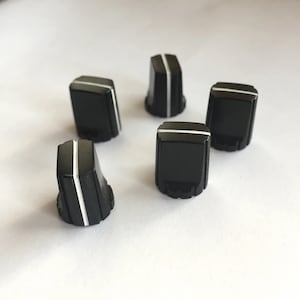 May include: Five black square-shaped knobs with a white line down the centre. The knobs are for use with electronic equipment.